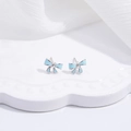 Close-up of light blue ribbon stud earrings on a white wavy ceramic tray - Blue Bow
