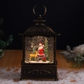 Primer plano de farol navideño de bronce con Papá Noel, renos y efecto de nieve real - Santa Claus
