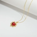 Close-up of golden necklace featuring a sunburst design with a red heart-shaped gemstone - Heart Pendant / Red