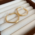 Dettaglio di orecchini quadrati in oro opaco esposti in una scatola portagioie in tessuto - Oro