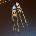 Primo piano macro degli orecchini a fiore vintage con zirconi e lunghe nappe dorate. - Stile Nappine Fiore Tre Petali Oro (40#)