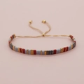 Makroaufnahme von buntem Tila-Perlenarmband mit verstellbarem Goldzugband und glatten Perlen - Rot Blau Gold Grau