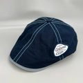 Detailed side view of navy blue flat cap with blue stitching and embroidered label - M / Blue