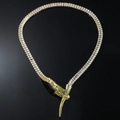 Détail de chaîne serpent dorée avec pierres et fermoir en forme de main sur fond noir - Doré