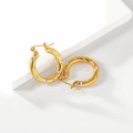 Detalle de pendientes de aro dorados con cristales transparentes sobre una piedra blanca - Dorado