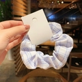 Blue and white plaid fabric scrunchie with a white hanging tag shown held by hand - Artistic Girl Blue Grid
