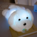White glowing plush dog toy with internal LED light lying on a book in warm dark setting - White Corgi / 50 cm