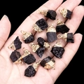 Set of thirteen black raw stone pendants with gold plated edges held in a palm - Black Tourmaline