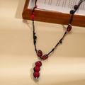 Dettaglio del ciondolo a baccello con perle rosse e cordoncino nero intrecciato - Stile Nero