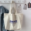 Close-up of canvas tote bag with blue slogan text hanging against a denim jacket - SOMEONE (No Charm)