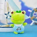 Primer plano de una rana de peluche verde con peto de delfín azul, estilo marinero - Rana Bordado Delfín / Azul / 12cm
