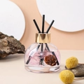 Detail view of the glass diffuser bottle with pink flowers, pine cones and black reeds - Set (Including Reed Sticks + Non-slip Mat) / White Peach Oolong