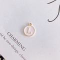 Detailed view of a round pink enamel pendant with gold-trimmed letter L on vintage paper - Letter L