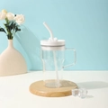 Close-up of a clear glass water bottle with white handle and straw on a wooden coaster - 20oz / White