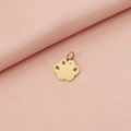 Detalle del colgante de huella dorada con cristal brillante sobre fondo de tela rosa - Dorado