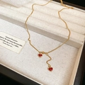 Detailed macro view of golden Y-shaped tassel necklace with red heart pendants in box - Gold Red