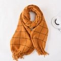 Orange knit scarf with black grid pattern and fringe details on a cozy setup - Orange