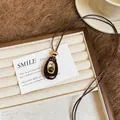 Dettaglio macro del ciondolo in resina marrone con anello dorato su cordino intrecciato - Caffè - Ovale