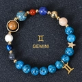 Macro shot of 8mm Gemini zodiac blue natural stone beads with gold charms on black - Gemini