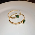 Detail view of golden bamboo C-shape earrings with green teardrop zircon on white plate - Gold Large Bamboo Hoop With Green Teardrop Gem