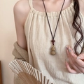 Detail der hölzernen Kürbis-Halskette mit rotem Knoten an Model im Zen-Leinenoutfit - Kaffee Kürbis Stil (5#)