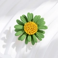 Macro view of green daisy brooch with textured yellow center on wavy white backdrop - Green Daisy