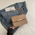 Khaki quilted chain crossbody bag with gold hardware on denim jacket and white bedding - Khaki