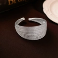 Detail of layered silver metal wire cuff bracelet with spherical ends on dark fabric - Multi-layer Geometric Style / Silver