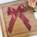 Detail of elegant red satin bow hair clip placed on a rustic wooden tray with soft lighting - Burgundy