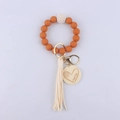 Dettaglio del portachiavi in silicone arancione con ciondolo mama in legno e nappa - Arancione
