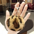 Leopard print plush heart keychain with silver metal ring held against a blurry background - Khaki Leopard Pom Pom