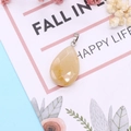 Macro shot of faceted yellow teardrop gemstone pendant with silver clasp on floral card - Topaz