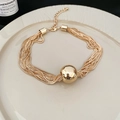 Detailed view of layered gold chain necklace with polished sphere pendant on ceramic dish - Necklace - Gold