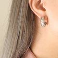 Silver croissant hoop earrings with ribbed texture design worn on model's ear - Steel
