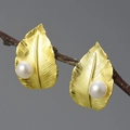 Elegant gold leaf earrings with white pearls displayed on a natural wood branch - Gold