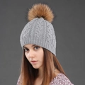 Detalle de gorro de lana de punto trenzado gris claro con pompón de pelo marrón suave - Gris + Pompón de Color Natural