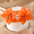 Vibrant orange acrylic flower earrings with golden centers on white ceramic cup - Orange
