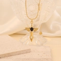 Collar de cruz dorada con alas de ángel y piedra negra sobre un vaso de cristal - Negro