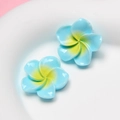 Detail shot of two blue resin plumeria flower charms with yellow center on white plate - Small Light Blue