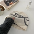 Berretto invernale in maglia beige con motivo a fiocco grigio su tavolo bianco - Berretto-Crema