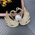 Detail of golden twin swan brooch with crystal pave setting and central large white pearl - BZ016 Heart Twin Swan