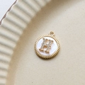 Detailed shot of a gold-plated shell pendant with H-letter zircon inlay on a ceramic tray - H Round