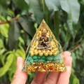 Orgonite pyramid with golden Buddha and green crystals on a natural garden background - Style 9