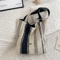 Striped fleece tote bag in black and beige with a metallic logo on a plush carpet - Wide Stripe
