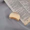 Detail of a golden metal hair claw clip with striped texture on a vintage book page - Brushed Gold Semicircle