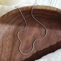 Macro shot of silver snake chain necklace on dark wooden tray with white textured fabric - Steel Color Round Snake Chain