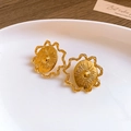 Boucles d'oreilles soleil dorées avec cadres ondulés posées sur une assiette blanche - Clous d'oreilles soleil entrelacé avec tige en argent