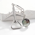 Macro detail of silver plane keychain with glass globe and integrated bottle opener - Pluto Galaxy