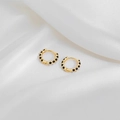 Detailed close-up of gold hoop earrings with black polka dots on white silk fabric - Black
