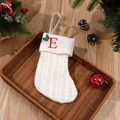 White cable knit Christmas stocking with red embroidered letter E and holly leaf decoration - Letter E